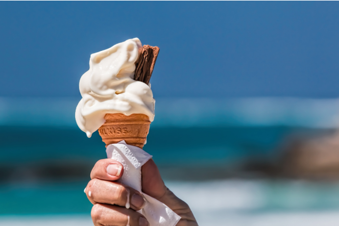 A Mr Whippy style ice cream with a chocolate flake being held up against the backdrop of the sea