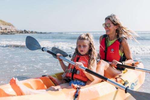 Mother and daughter smile and laugh as they kayak together on the sea in the sunshine
