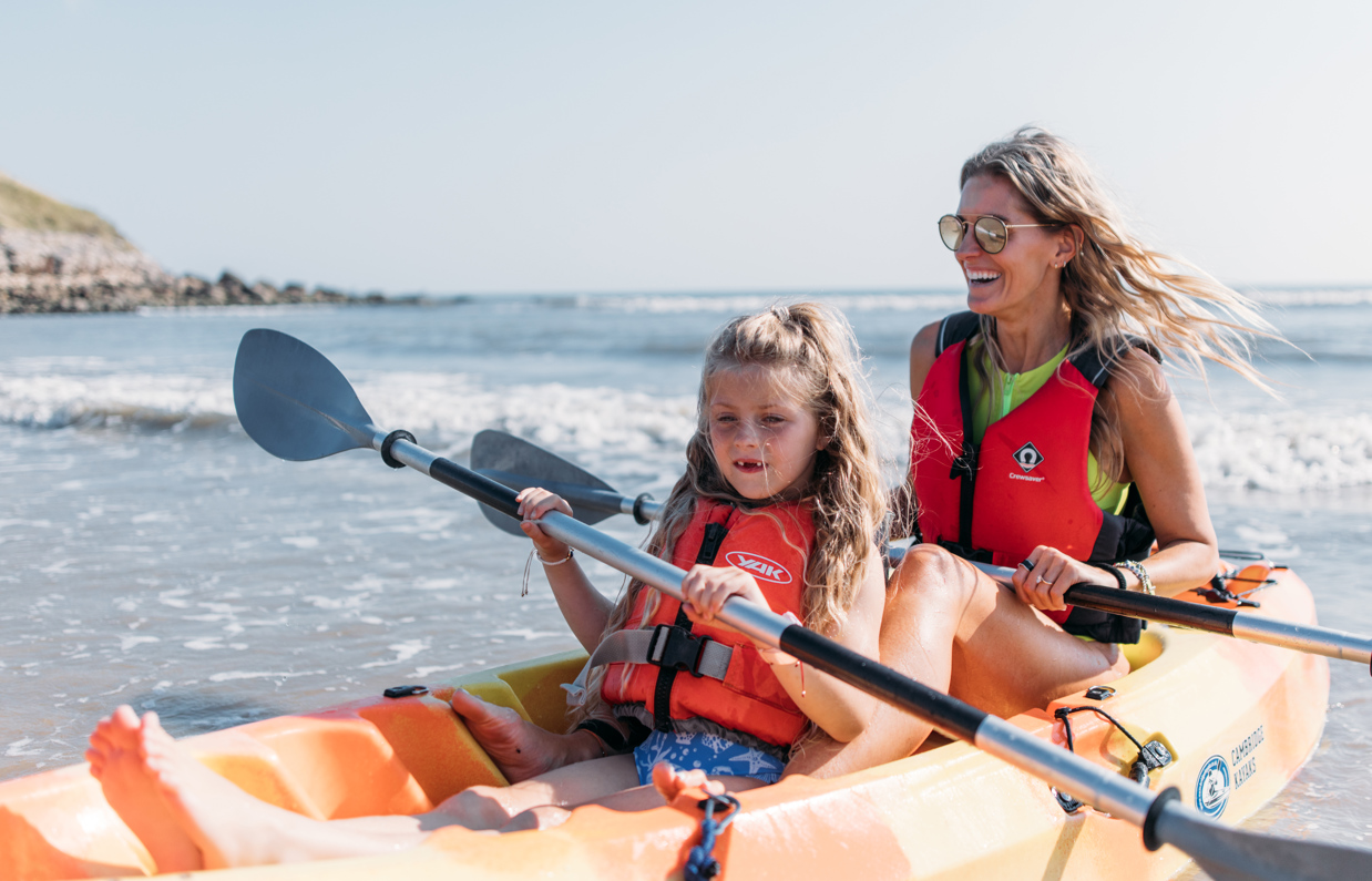 Mother and daughter smile and laugh as they kayak together on the sea in the sunshine