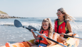 Mother and daughter smile and laugh as they kayak together on the sea in the sunshine