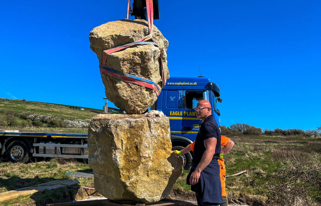 Installation of a stone sculpture in a field with blue skies