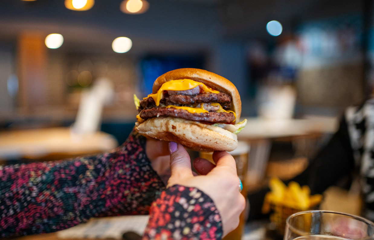 A woman's hands holding a double cheese and bacon burger