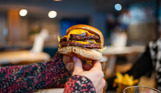 A woman's hands holding a double cheese and bacon burger