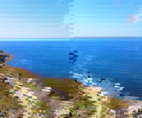 A rocky coast path with a female walking along and views of the blue sea