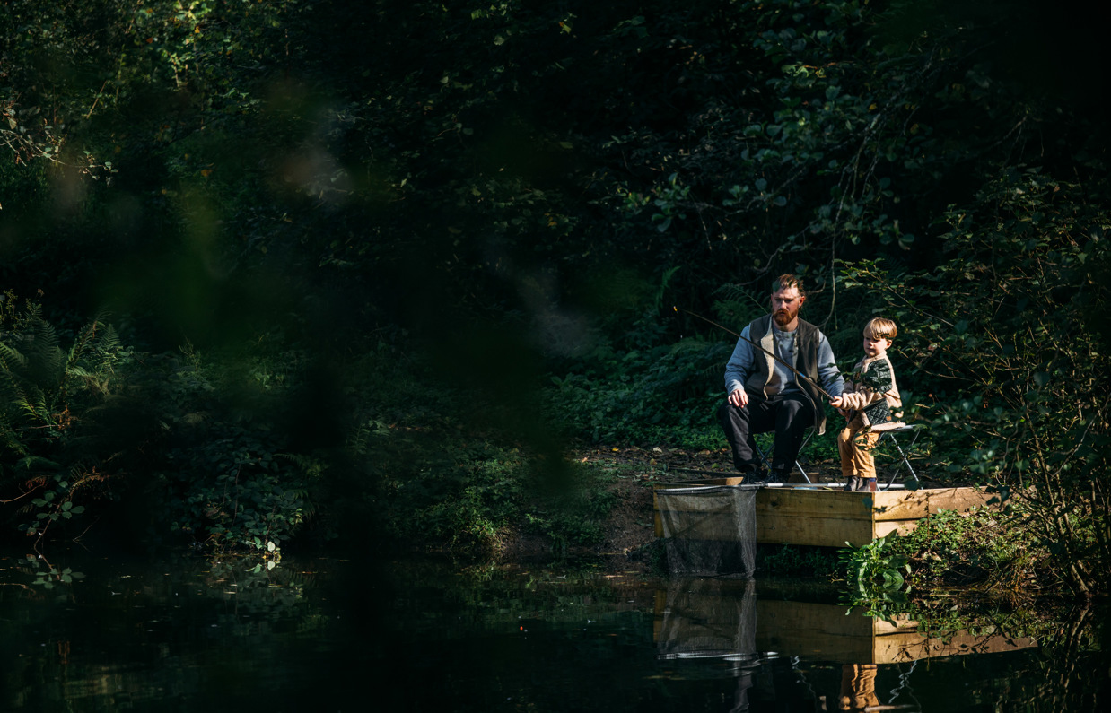 A man and his young son fishing by a lake in the woodland 