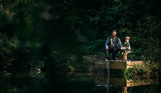 A man and his young son fishing by a lake in the woodland 