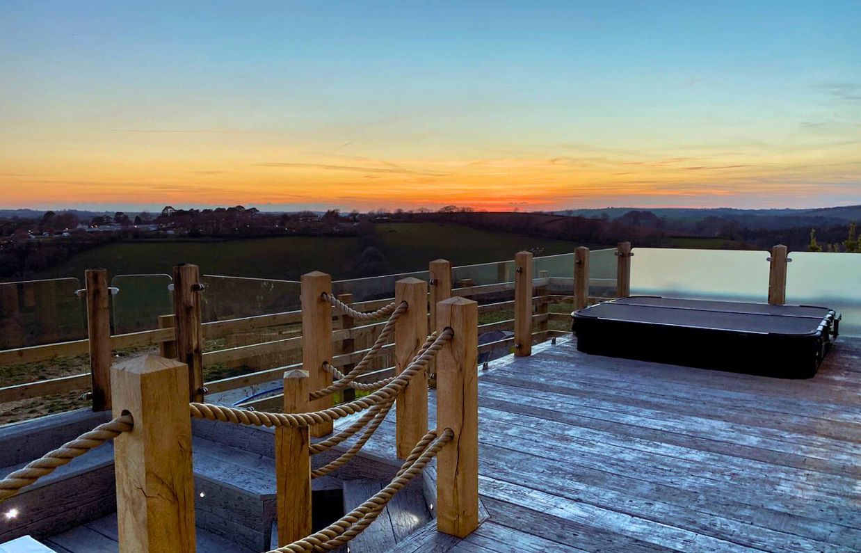 External of a luxury lodge decking with sunken fire pit, sunken hot tub and countryside views at sunset