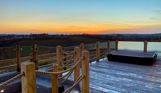 External of a luxury lodge decking with sunken fire pit, sunken hot tub and countryside views at sunset