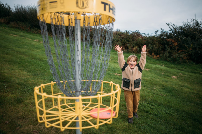 A Young Boy Celebrating Playing Frisbee Golf in a Field 