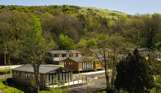 Holiday lodges among woodland at the bottom of rolling countryside hills on a sunny, blue sky day