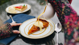 Two desserts on an outdoor table, one of which a treacle tart with custard being poured over the top