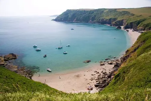 A small bay at the bottom of rolling countryside hills with various boats in blue water