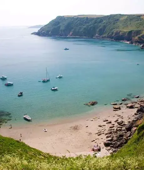 A small bay at the bottom of rolling countryside hills with various boats in blue water