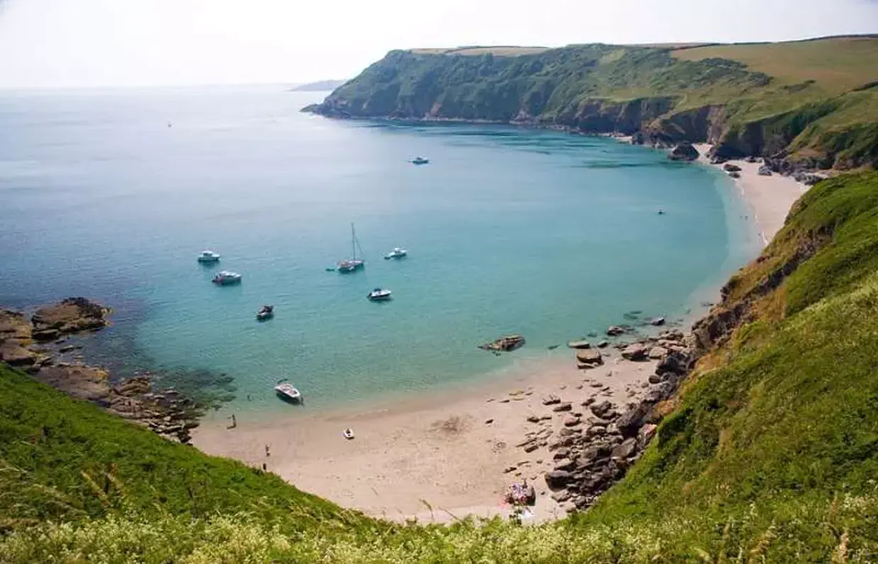 A small bay at the bottom of rolling countryside hills with various boats in blue water