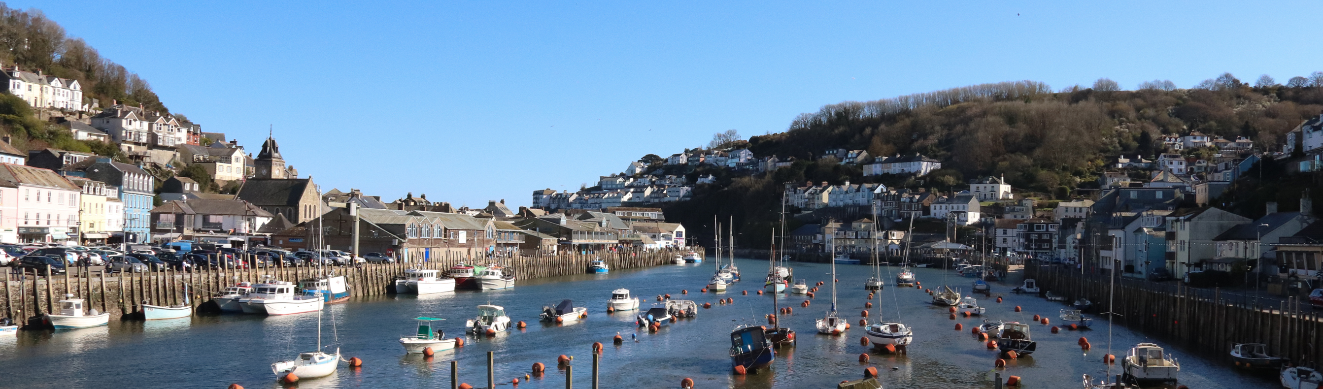 Looe Harbour with various ships on the water on a sunny, blue sky day