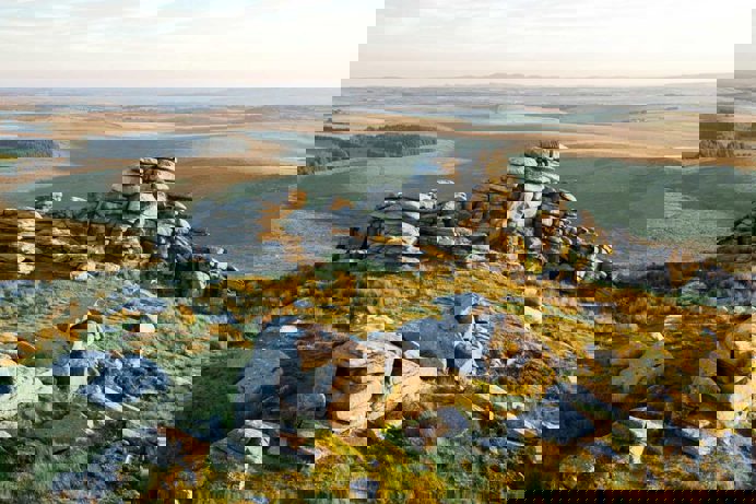 A vast view of countryside and rolling hills with rock piles in the foreground