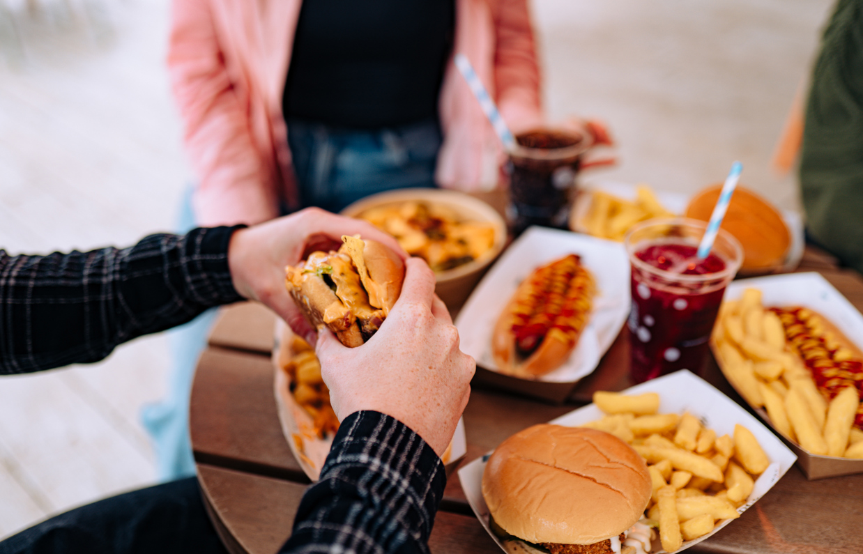 A selection of street food burgers and hot dogs with drinks and a burger being picked up by a man's hands