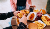 A selection of street food burgers and hot dogs with drinks and a burger being picked up by a man's hands
