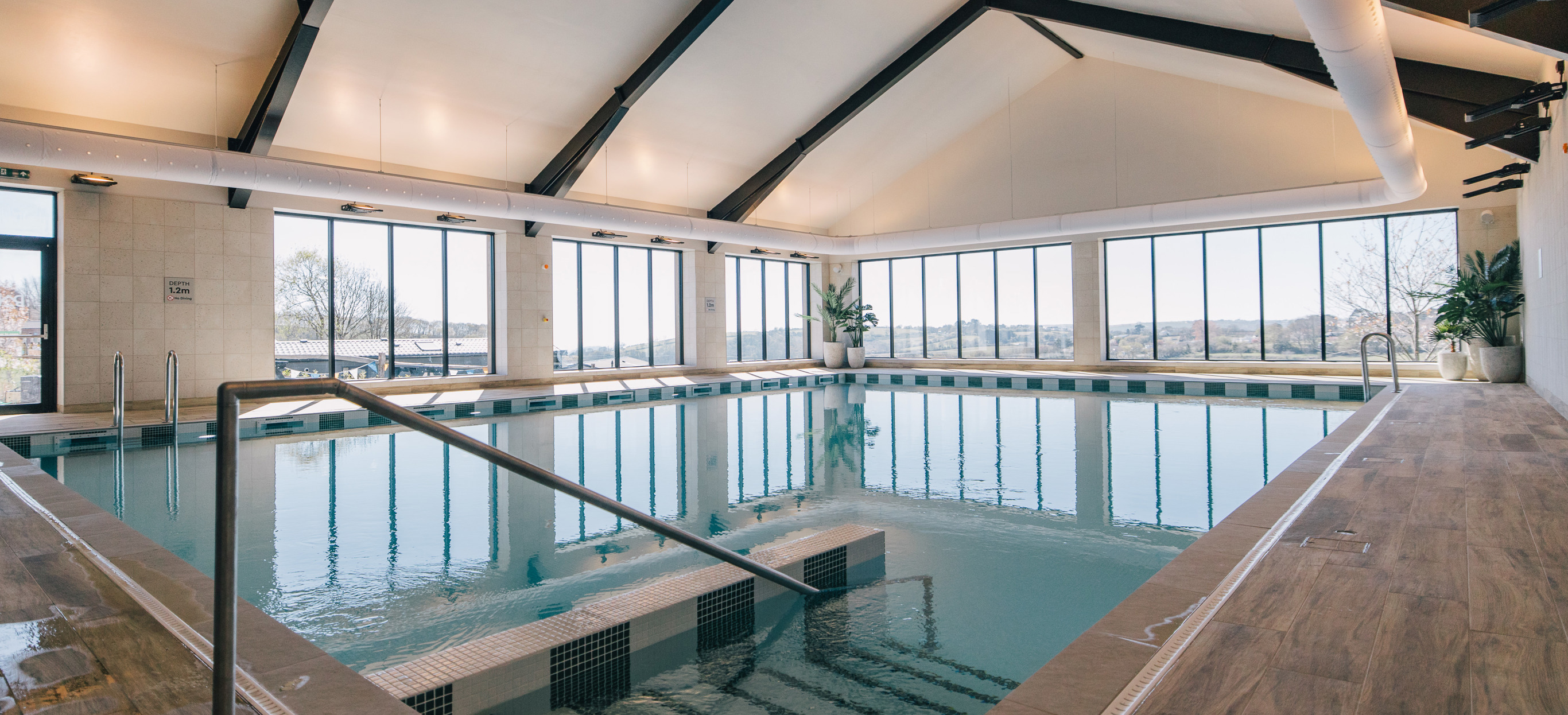 An indoor heated swimming pool within a barn style building with boho-chic styling and countryside views