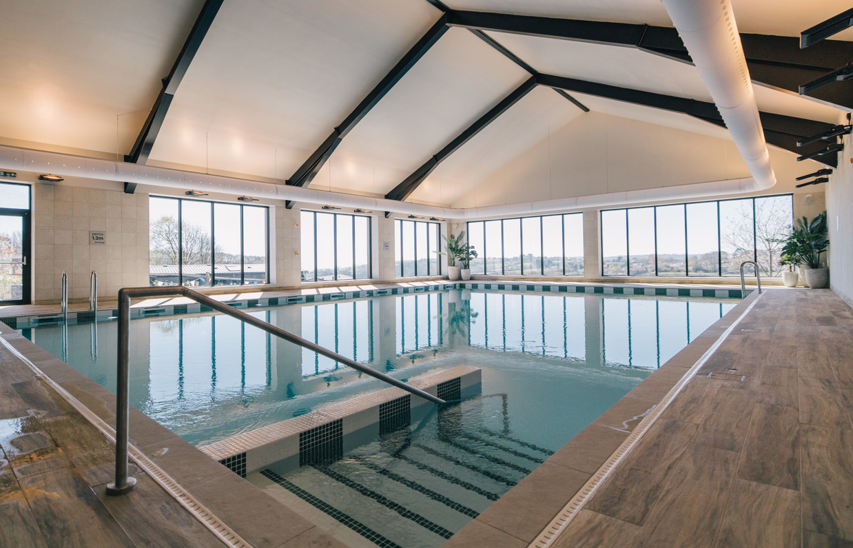 An indoor heated swimming pool within a barn style building with boho-chic styling and countryside views