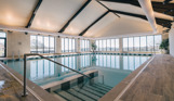 An indoor heated swimming pool within a barn style building with boho-chic styling and countryside views