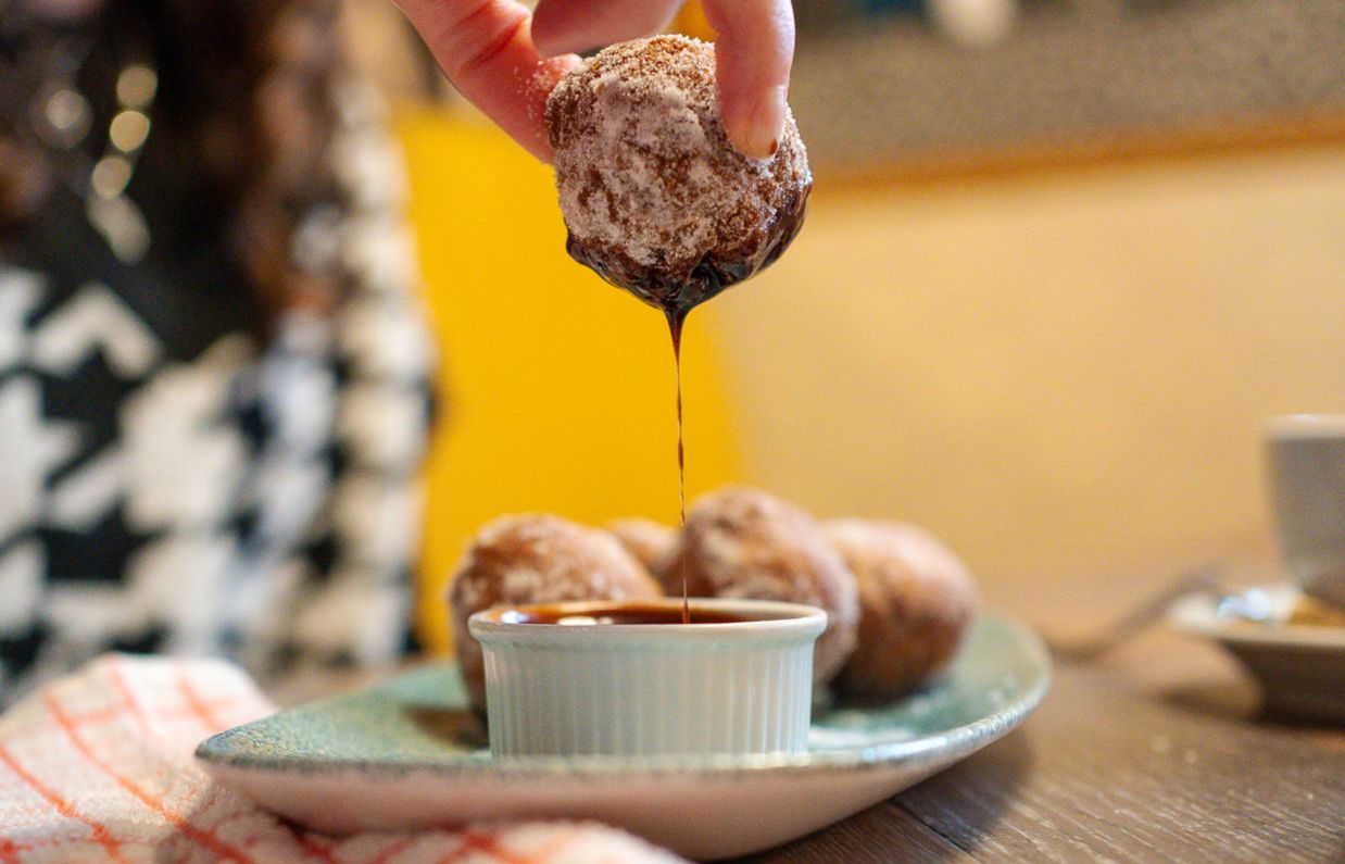 A mini donut dunked in chocolate sauce dripping from the bottom