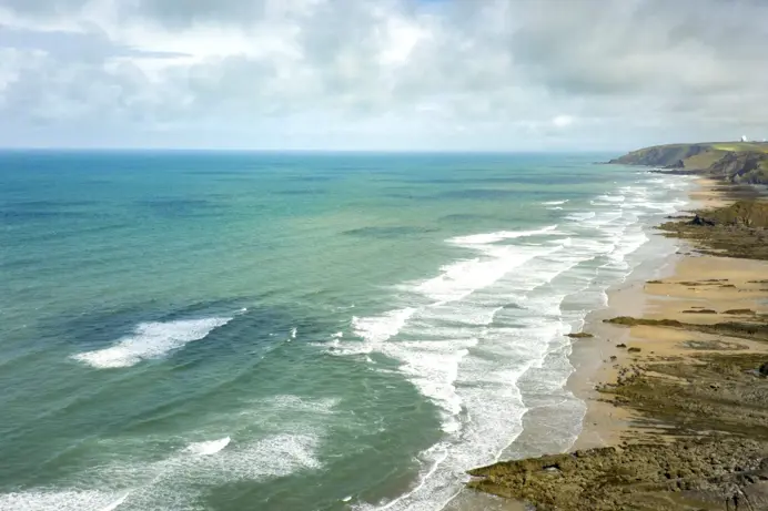 A long stretch of coastline at high tide with grassy headland
