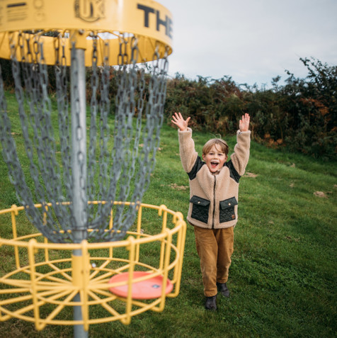 A young boy celebrating getting a disc in the goal in the disc golf course in a field