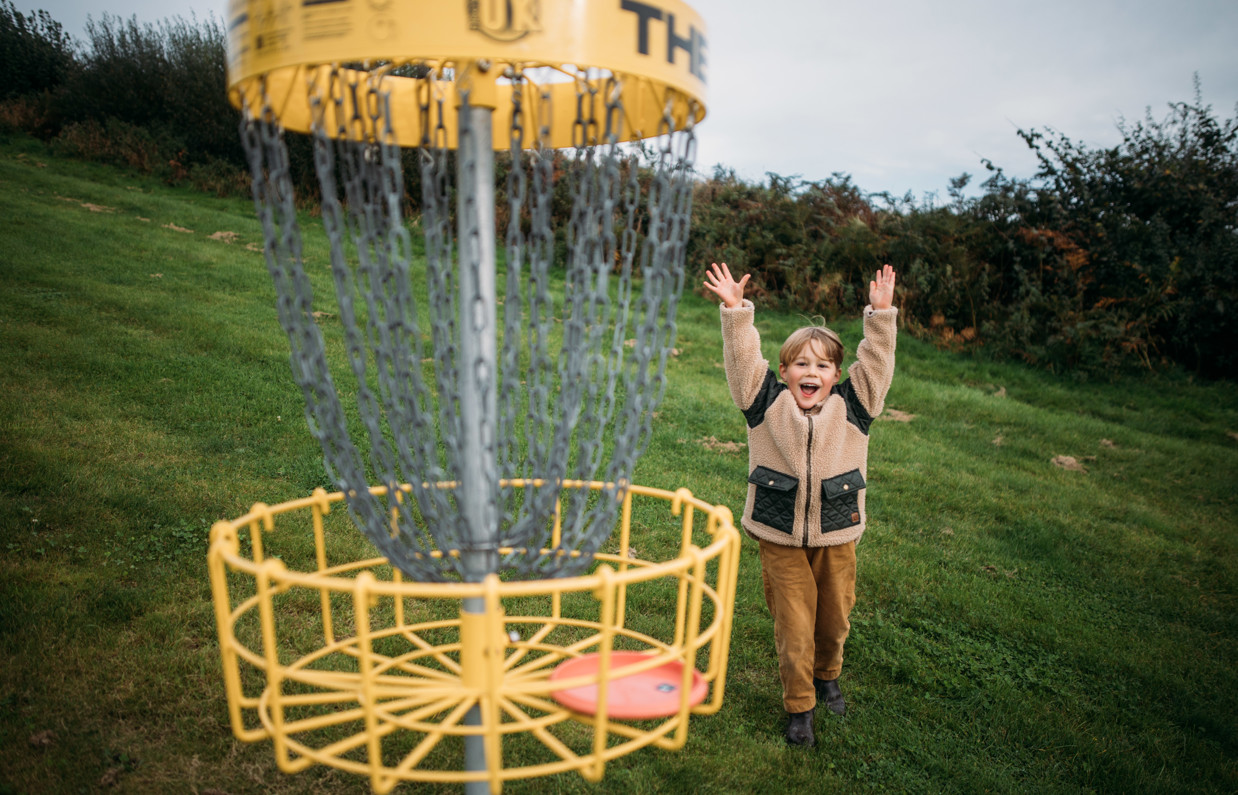 A young boy celebrating getting a disc in the goal in the disc golf course in a field