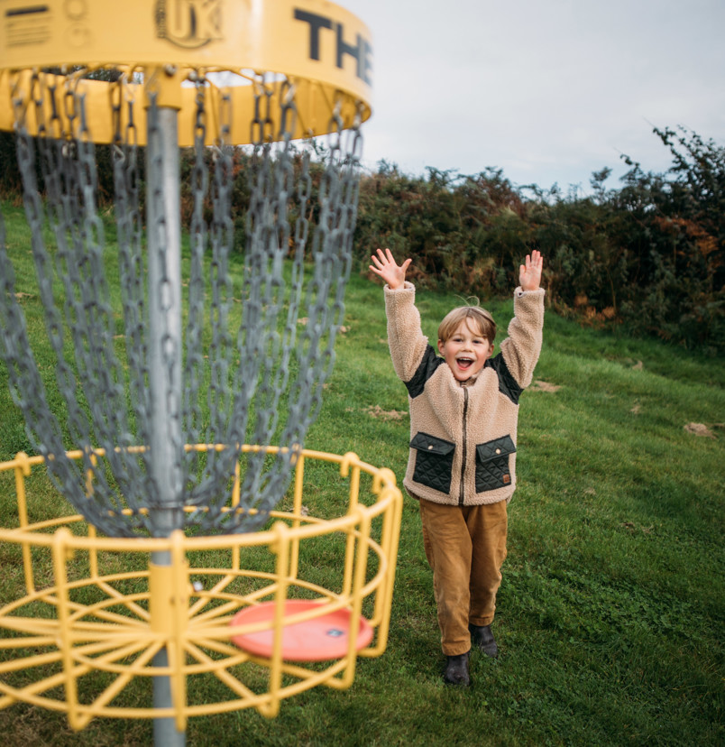 A young boy celebrating getting a disc in the goal in the disc golf course in a field