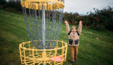 A young boy celebrating getting a disc in the goal in the disc golf course in a field