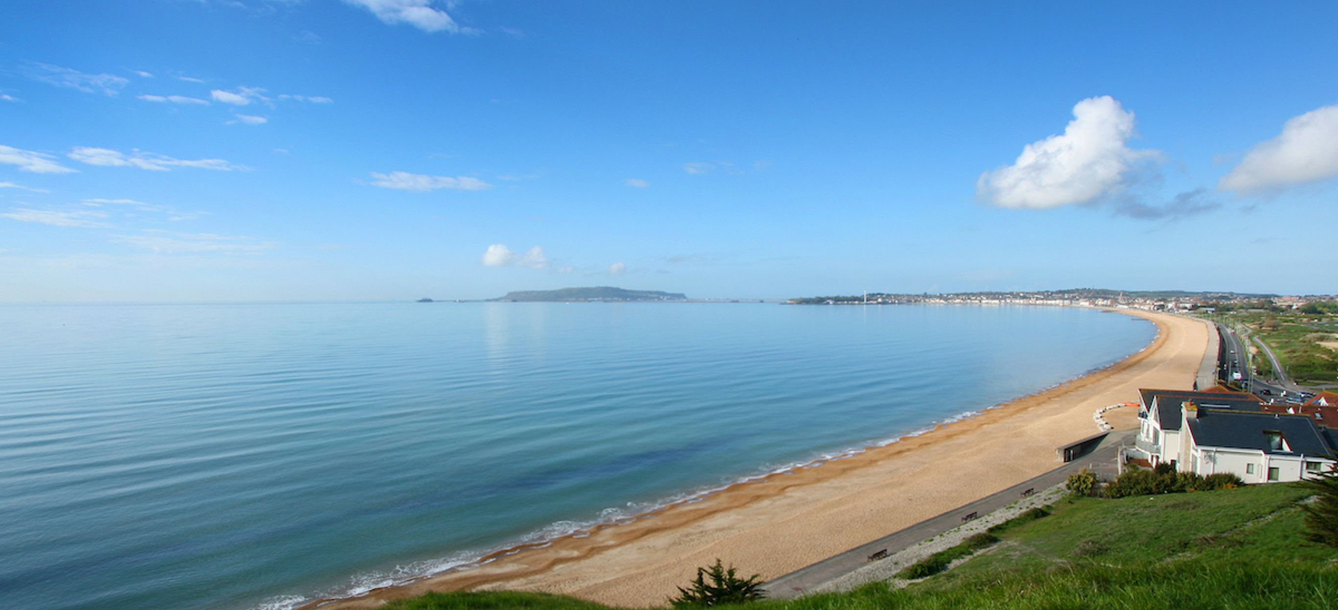 The view of sweeping Weymouth Bay on a sunny, blue sky day with serene blue water