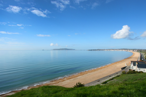 The view of sweeping Weymouth Bay on a sunny, blue sky day with serene blue water
