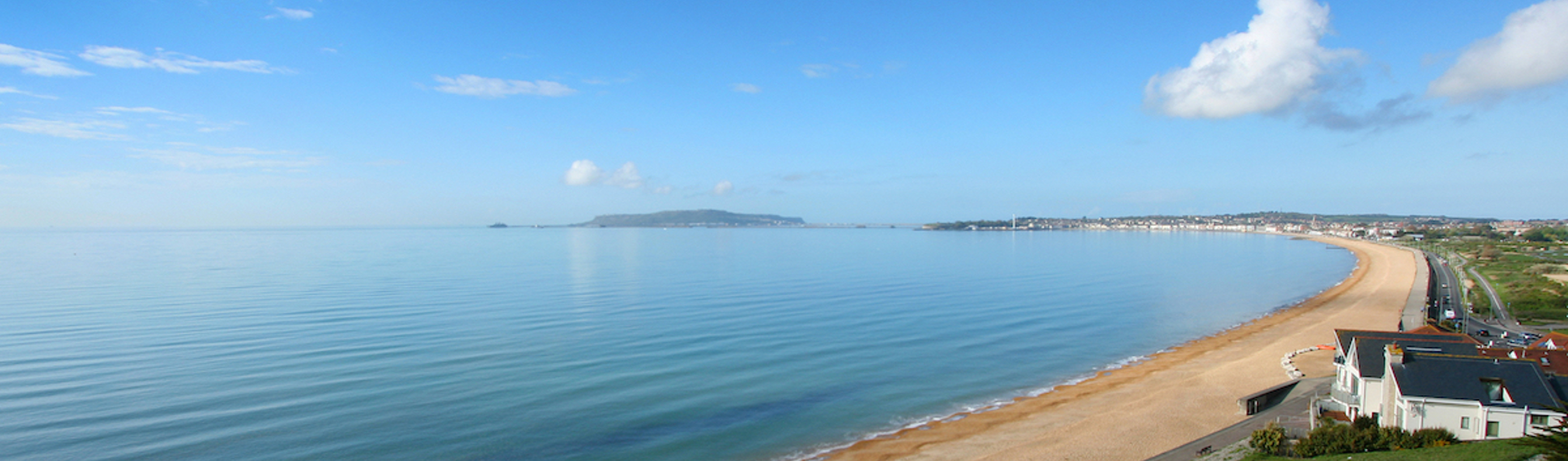 The view of sweeping Weymouth Bay on a sunny, blue sky day with serene blue water
