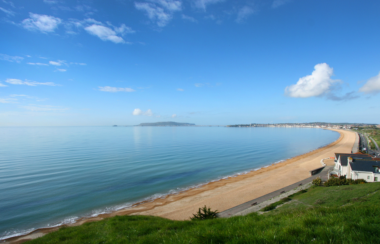 The view of sweeping Weymouth Bay on a sunny, blue sky day with serene blue water