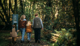 A family of four walking along a nature path among woodland in the sun