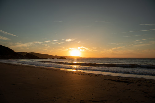 The sunset over a beach with calm seas and dramatic cliffs