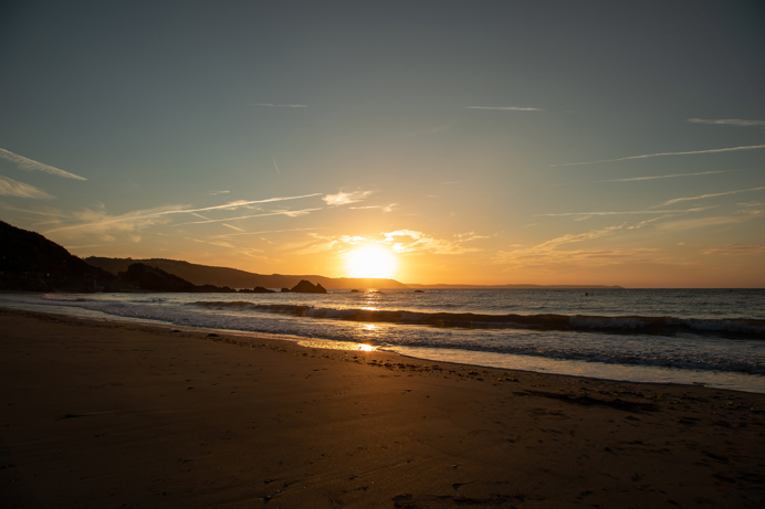 The sunset over a beach with calm seas and dramatic cliffs