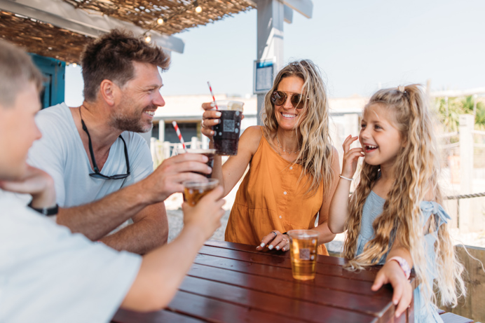 A couple with a young girl and boy at a table outside toasting drinks and smiling