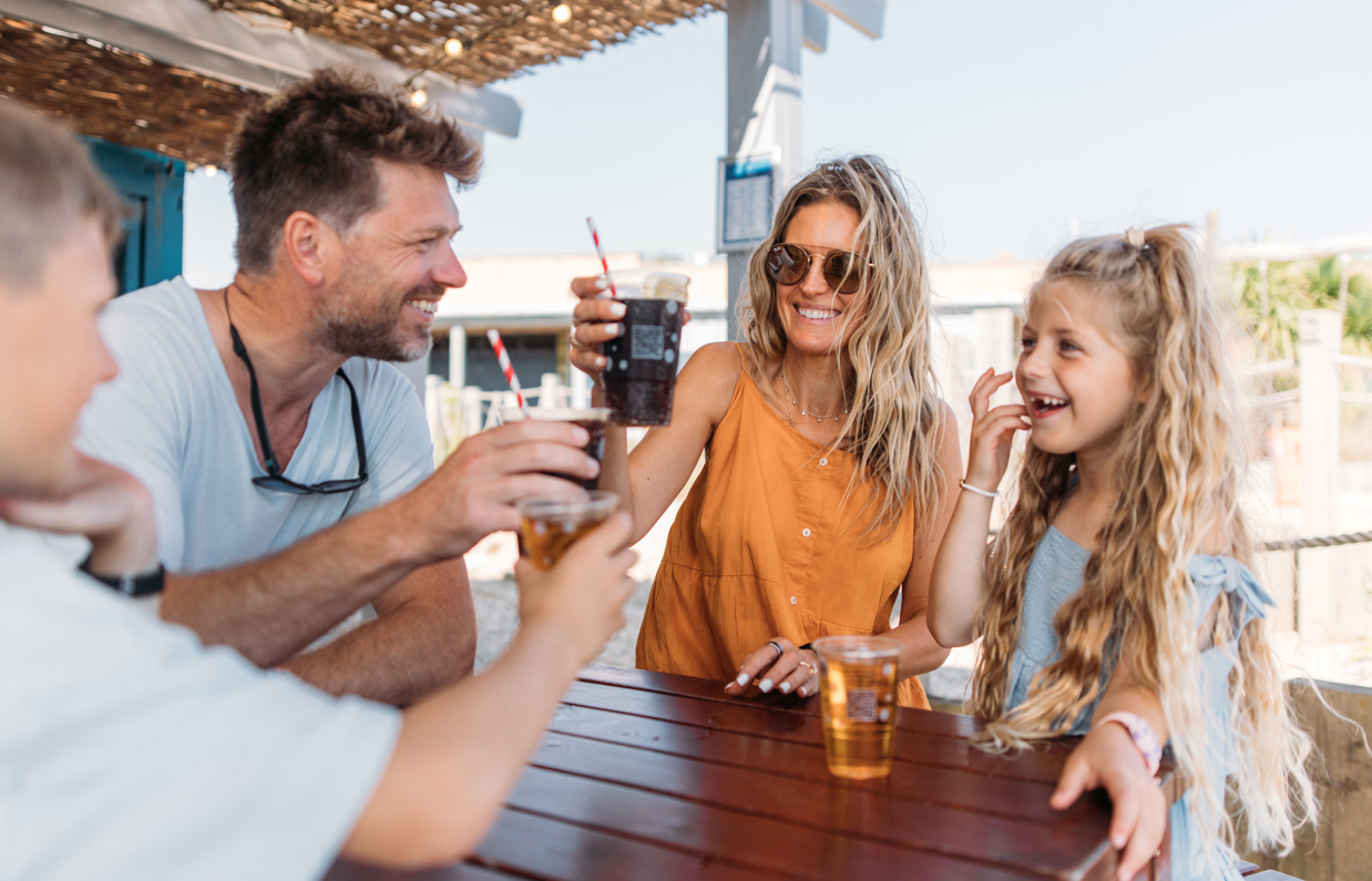 A couple with a young girl and boy at a table outside toasting drinks and smiling
