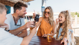 A couple with a young girl and boy at a table outside toasting drinks and smiling