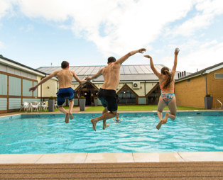 A man and two kids jumping into a heated outdoor pool on a sunny day