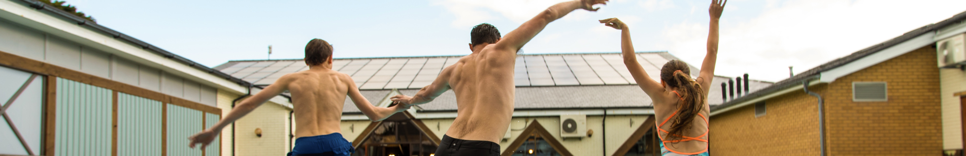 A man and two kids jumping into a heated outdoor pool on a sunny day