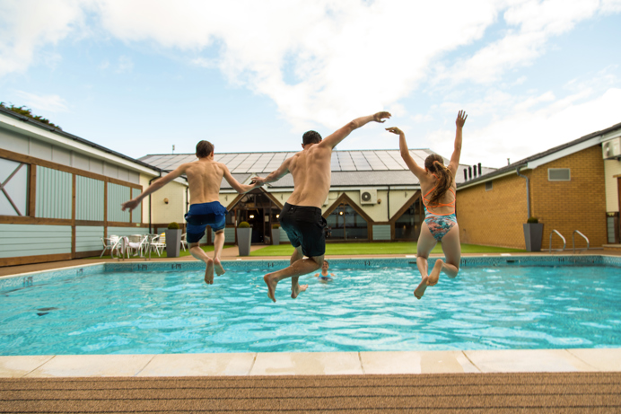 A man and two kids jumping into a heated outdoor pool on a sunny day