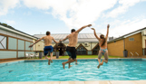 A man and two kids jumping into a heated outdoor pool on a sunny day