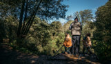 A man and his two young sons sat by a lake in the woodland setting up fishing gear