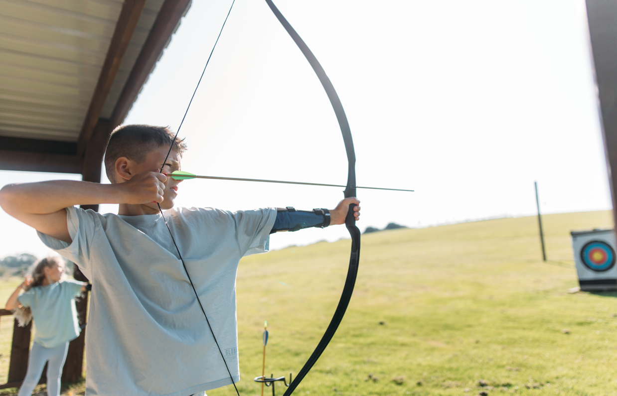 A young boy in a field aiming an archery bow at target