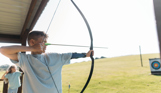 A young boy in a field aiming an archery bow at target
