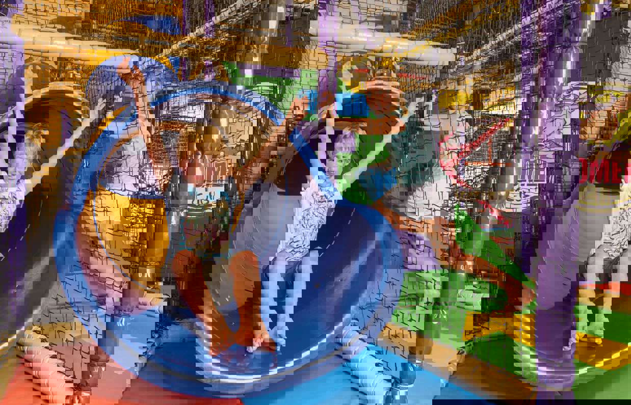 A young boy and girl playing in an indoor play area with climbing apparatus and slide