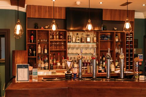 A moody decor bar with wooden features and pendant lights above a set of draught beers as well as spirits and other drinks